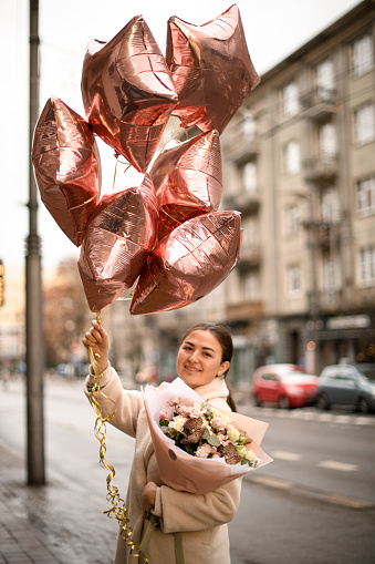 pretty woman outdoor holding lush bouquet of flowers and bunch of shiny helium balloons. Happy birthday concept
