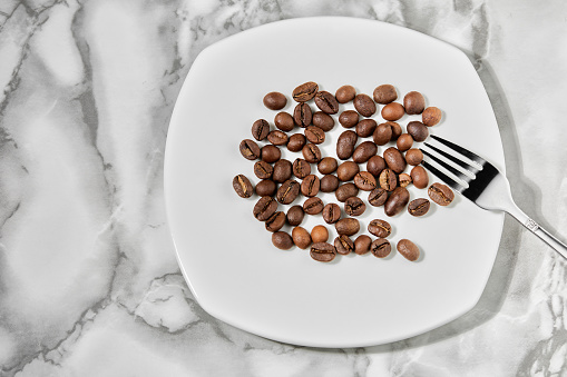 roasted aromatic coffee beans are scattered on a white plate top view