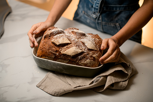 view on tasty freshly baked sourdough bread in bakery form which female hands holds. Homemade bread food photography.