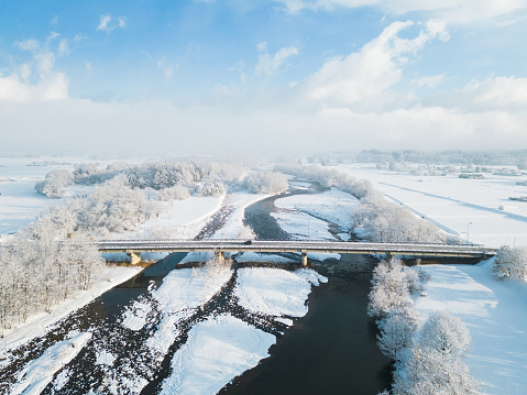 An early morning aerial view of a snowy North Japan rural landscape with bridge crossing a river and one small vehicle can be seen.