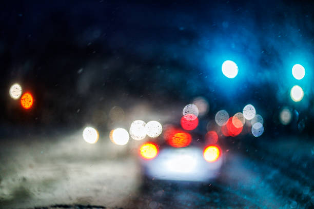 Abstract winter snow storm headlights, tail lights and traffic lights viewed through car windshield at night.