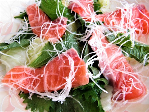Salad from raw salmon, lettuce, daikon, and shiso leaves. Close-up.
