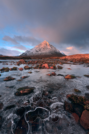 Landscape of the snow-covered Buachaille Etive Mor Mountain and the frozen Coe River at sunrise. Ice on the river in the foreground. Scottish Highlands, UK.