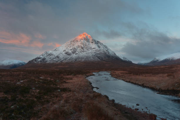 Landscape of the snowcapped Buachaille Etive Mor mountain and the Coe River at sunrise stock photo