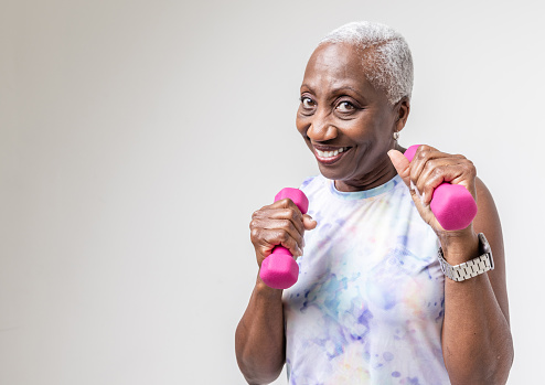 Portrait of a black woman with dumbbells against a light wall