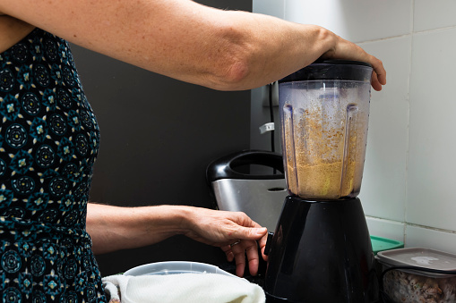 Young woman putting ingredients into a blender. Gastronomy at home. Salvador, Bahia, Brazil