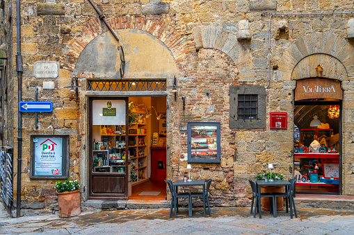 The entry and facade of a traditional Italian store and cafe in the historic medieval center of the Tuscan walled city of Volterra, Italy.