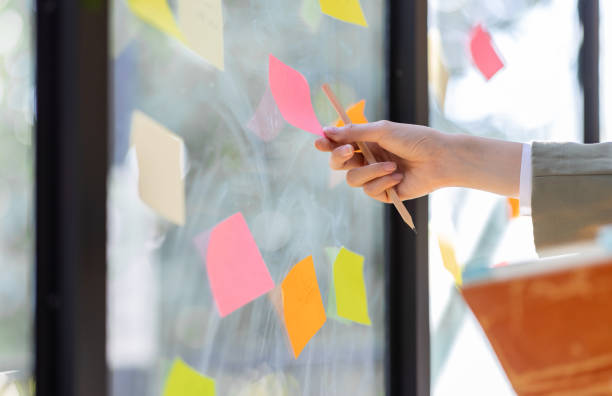 istock Young Asian woman Creative team use post it notes to share idea sticky note on glass wall. Asian business people design planning and Brainstorming thinking sticky History notes concept. 1471329866