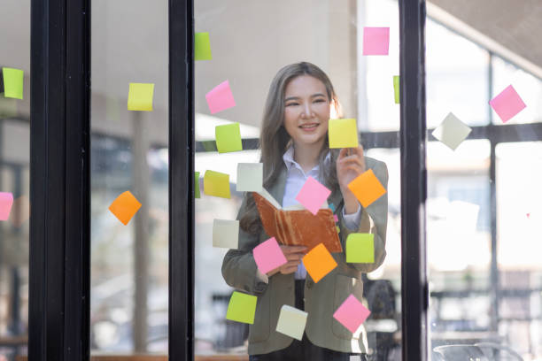 istock Young Asian woman Creative team use post it notes to share idea sticky note on glass wall. Asian business people design planning and Brainstorming thinking sticky History notes concept. 1471329882