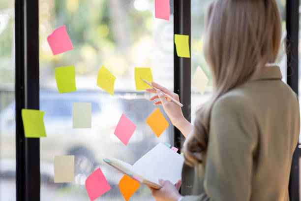 istock Young Asian woman Creative team use post it notes to share idea sticky note on glass wall. Asian business people design planning and Brainstorming thinking sticky History notes concept. 1471329886