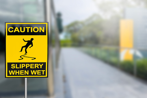 Warning sign of Caution Slippery When Wet on sidewalk on bright yellow on sidewalk  defocus background. Danger and safety concept.