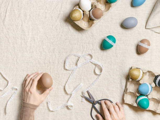 istock Decoration Easter eggs, female hands decorating colorful chicken egg with white tape lace, traditional celebration food and holiday symbol.  Home preparing for Happy Easter. Top view 1471339673