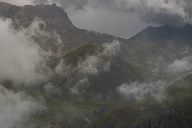 istock Stormy dramatic weather in mountain with fluffy grey clouds above high rocky ridges with green slopes and deep gorge in summer. Mountain landscape in bad weather. 1471354608