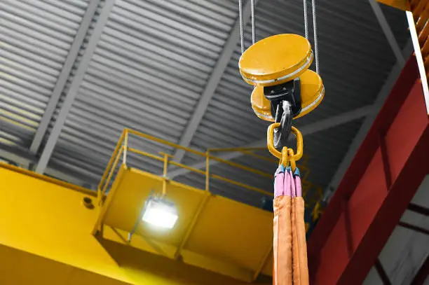Hook assembly with rigging and strops of moving crane hangs under ceiling in spacious workshop of plant close low angle shot