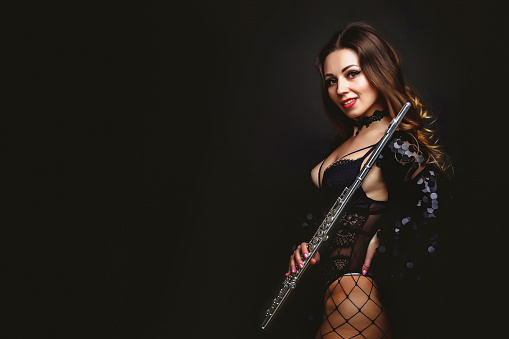 Stylish cover lady flautist posing with flute at black isolated background, looking at camera. Chic woman artist in black dress hold flute in hands. Orchestra music concept. Copy ad text space, banner