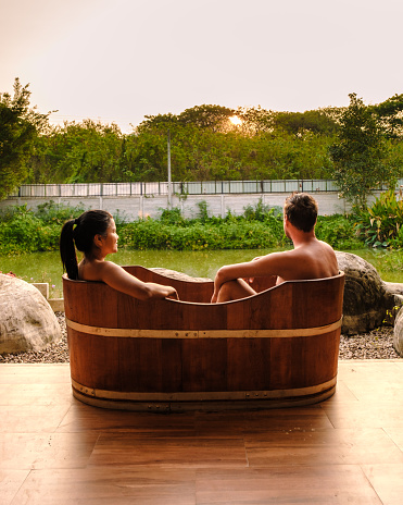 couple men and women in wooden bathtub at the countryside of Thailand watching sunset.