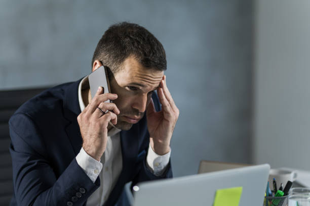 istock Worried businessman talking on mobile phone while working on laptop in the office. 1471361984