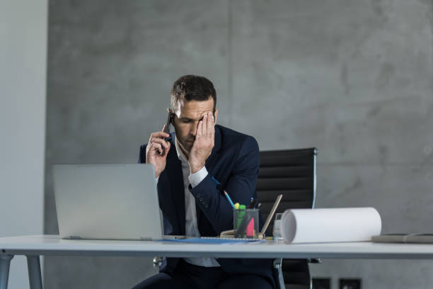 Worried businessman talking on mobile phone and covering his face in the office. stock photo