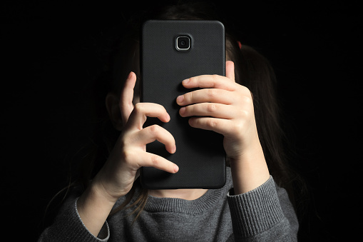 A large smartphone in children's hands, because of which the face is not visible. Kid gadget addiction and insomnia, psychological problems.