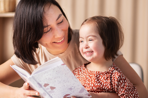 happy mother and daughter with down syndrome read a book, look at pictures, smile
