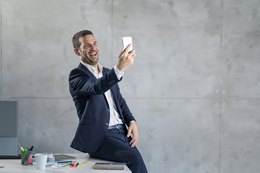 Cheerful mid adult businessman taking a selfie with mobile phone in the office. Copy space.
