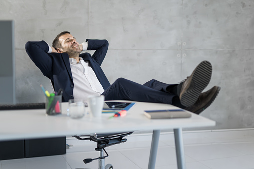 Happy male entrepreneur resting with his feet on the table and hands behind head in the office.