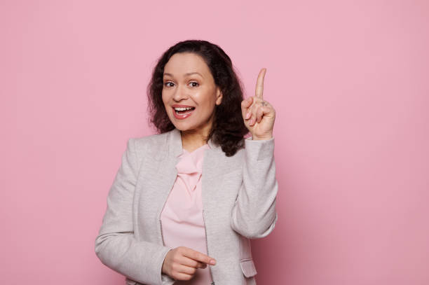 istock Charming woman pointing her index finger up, expressing idea and finding solution, smiling at camera, on pink background 1471365652