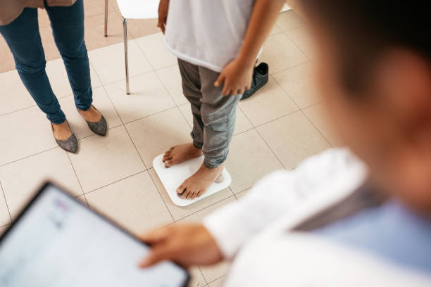 asian family with teenage boy visiting general practitioner, checking the boy's weight on weight scales - dieting weight scale doctor patient imagens e fotografias de stock