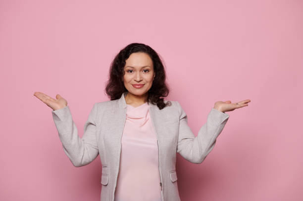 istock Smiling charming woman in light gray jacket, keeping her hands palms up, looking at camera, isolated on pink background 1471367695