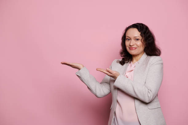 istock Charming middle-aged brunette woman, holds imaginary copy space for ads on her hands palms up, isolated pink background 1471367778