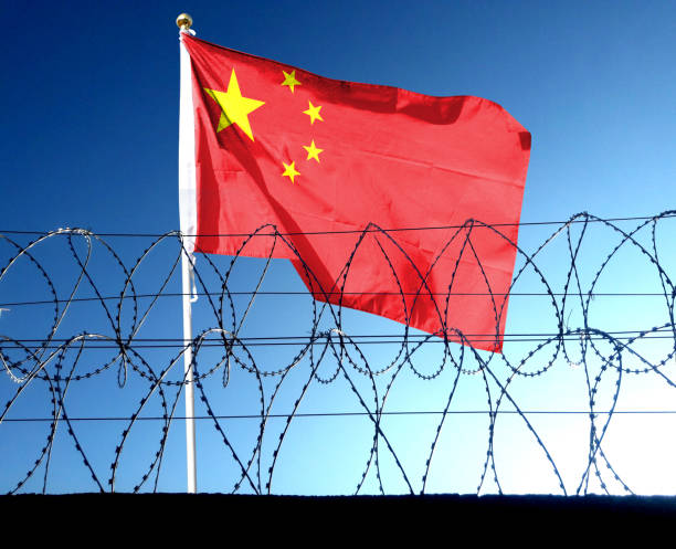 The Chinese flag hangs in the cloudy sky outside the prison's barbed wire. waving in the sky The Chinese flag hangs in the cloudy sky outside the prison's barbed wire. waving in the sky prc stock pictures, royalty-free photos & images