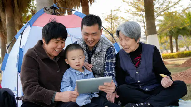 The little boy watches a tablet with his parents and great-grandparents