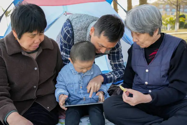 The little boy watches a tablet with his parents and great-grandparents