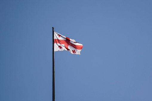 National flag of Georgia waving under blue sky.