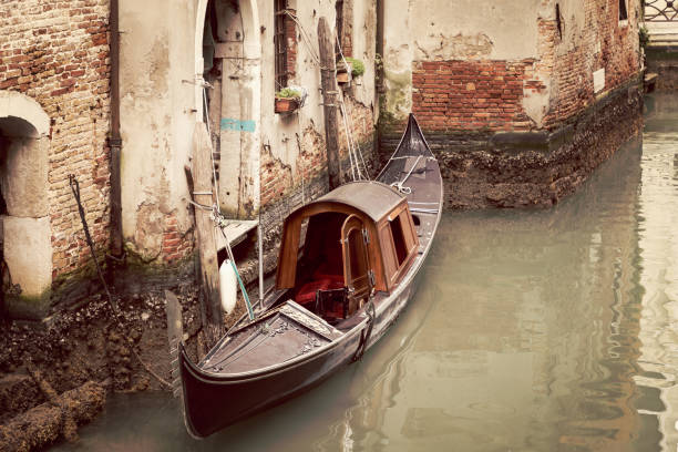 una vecchia gondola su un canale di venezia ormeggiata a una stretta uscita stradale (foto in stile vintage) - venice italy ancient architecture creativity foto e immagini stock