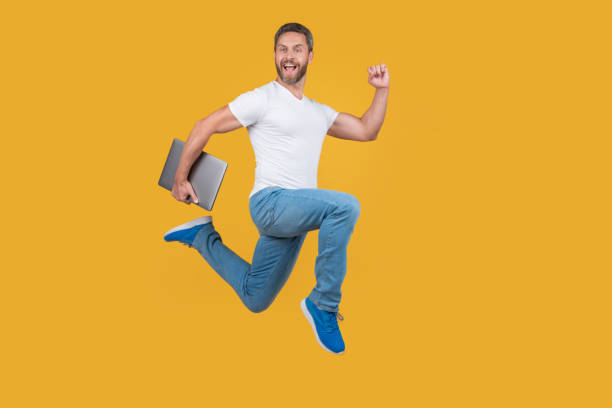 istock man running with laptop has deadline. Happy man midair yellow background. 1471379355