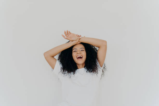 istock Overjoyed curly haired young lady keeps both hands on forehead, opens mouth and laughs happily, feels energetic, dressed in casual wear, poses against white studio background. What funny joke! 1471380084