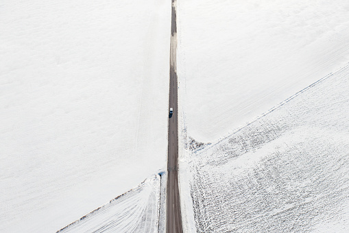 A van travelling on a road between fields covered in snow in the countryside.