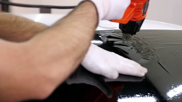 Master installs a tinting film on the car glass with a hair dryer and a spatula.