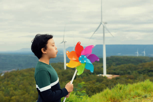 niño asiático progresivo jugando con un juguete de molinete de viento en una granja de turbinas eólicas. - run of the mill fotografías e imágenes de stock