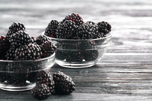 Blackberries in bowls on a light background on a wooden table, close-up shot