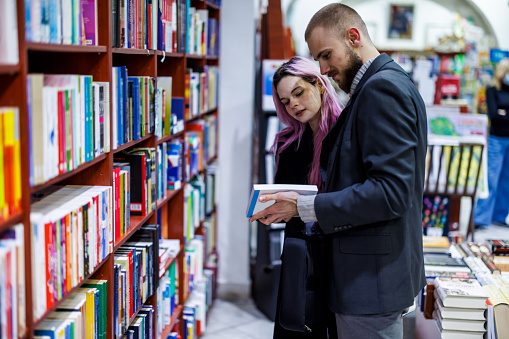 A young modern couple is looking through a library of books in the large section of a bookstore.