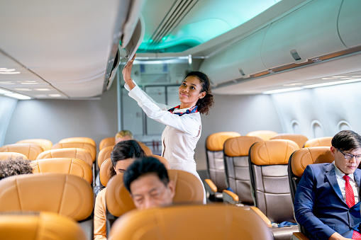Air hostess walk to close luggage compartment of airplane before take off and bring the passenger to the destination with happiness.