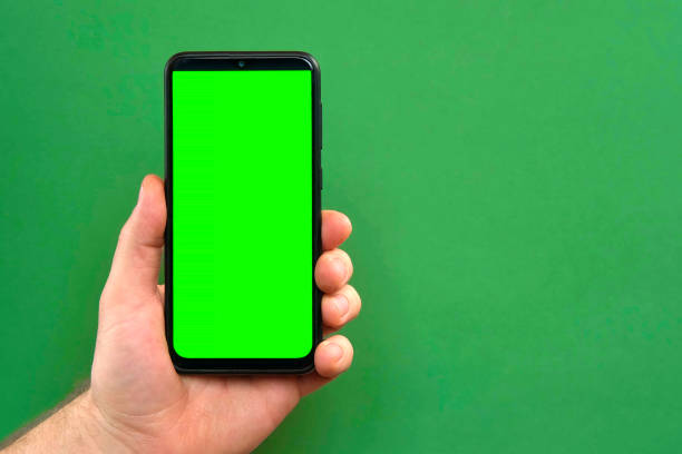 istock Mobile phone in young man hand. Use smartphone with blank green screen on green color studio background. Male showing black phone with chroma key display. Close up. Mock up of smart phone for Ad, app 1471395359