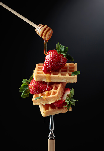 Waffles with strawberries and honey on a black background.