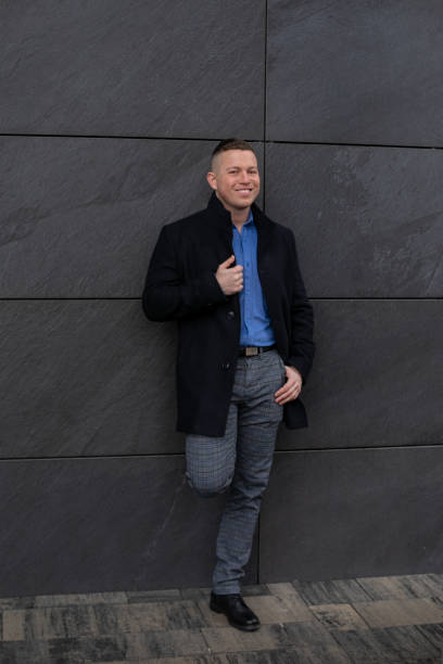 istock Full-length image of young attractive architect, dressed in black coat, standing against gray wall of city building. 1471397404