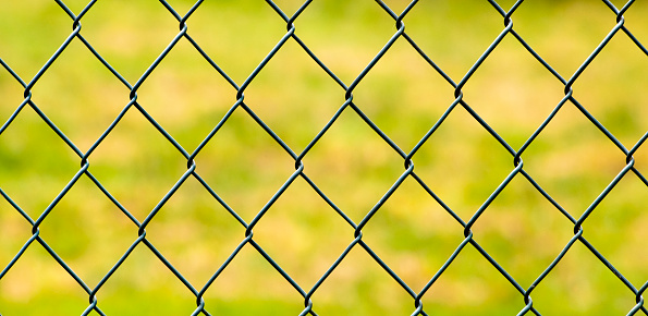 Full frame view of wire fence, green grass  brightly lit background.