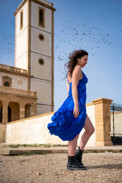 Photo of Grace of the Wind: A Blue-Dressed Woman with Her Dress Fluttering Next to a Dreamy Church