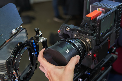 A caucasian videographer's hand installs an 85mm lens on a professional movie camera. High quality photo