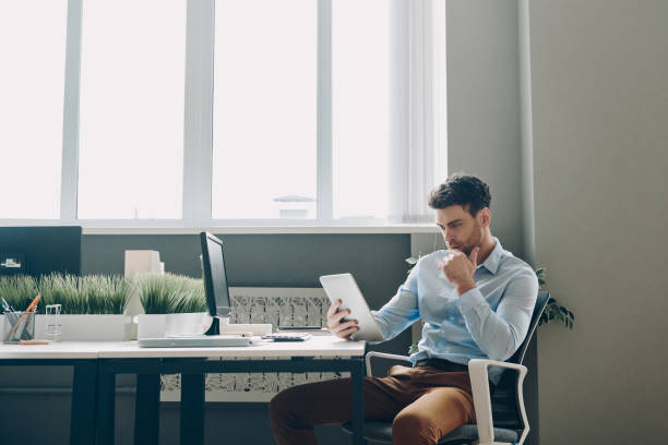 istock Thoughtful young businessman using digital tablet while sitting at his working place in office 1471405654